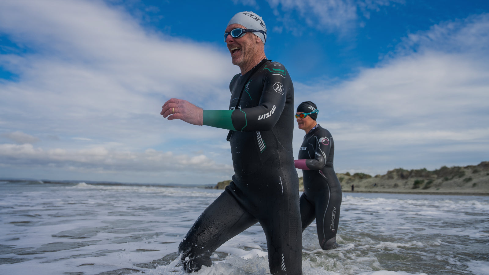Ein Mann und eine Frauen laufen lachend im Neoprenanzug ins Meer