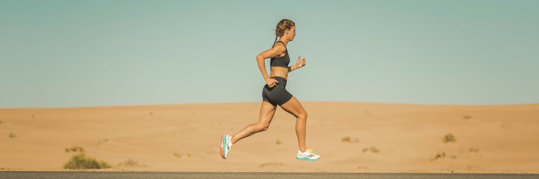 Eine Läuferin in kurzer Laufbekleidung beim Tempolauf auf einer einsamen Straße, Ansicht von der Seite