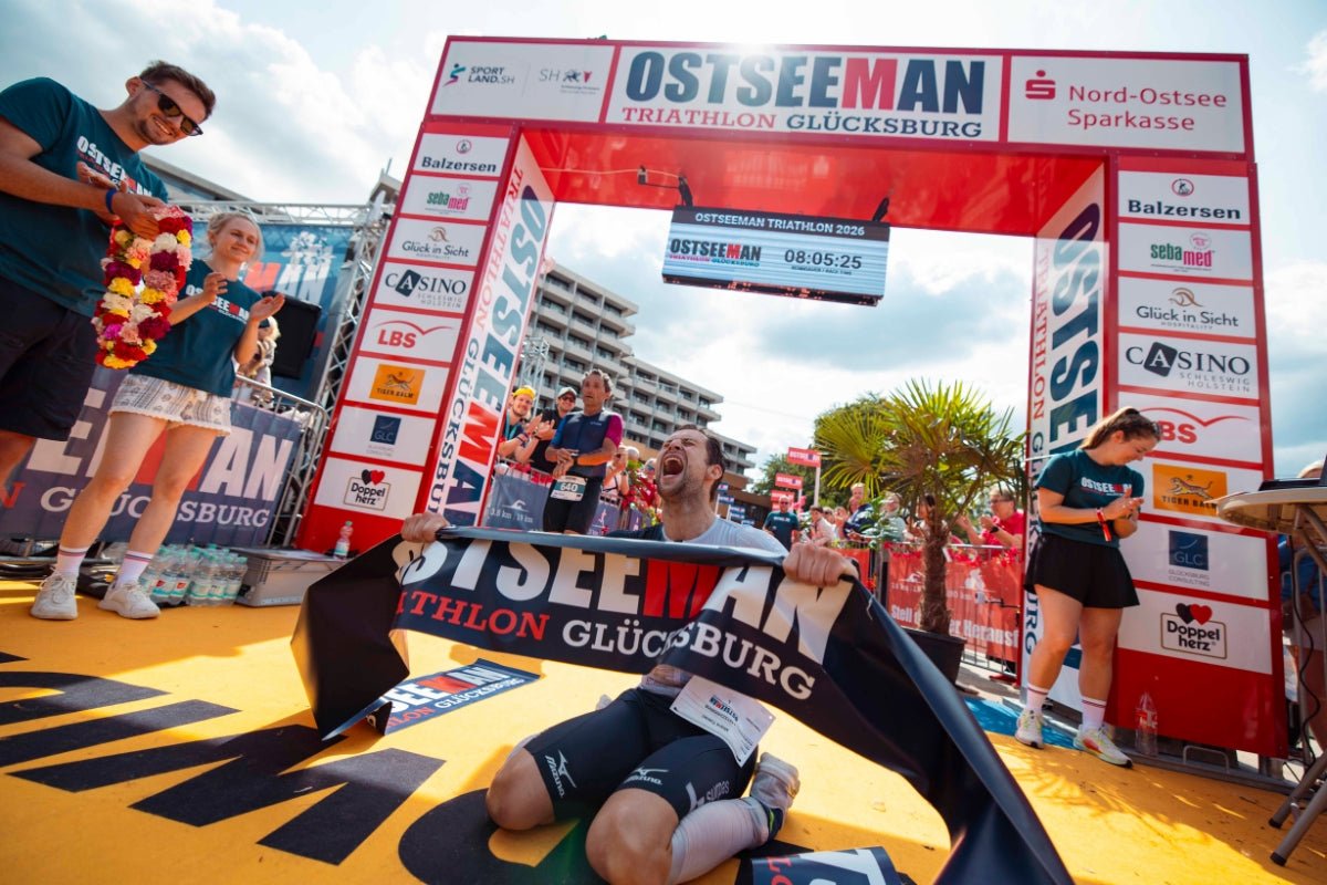 Lukas Schnödewind gewinnt den OstseeMan 2026 mit neuer Rekordzeit und wird im Ziel beim Jubel fotografiert.