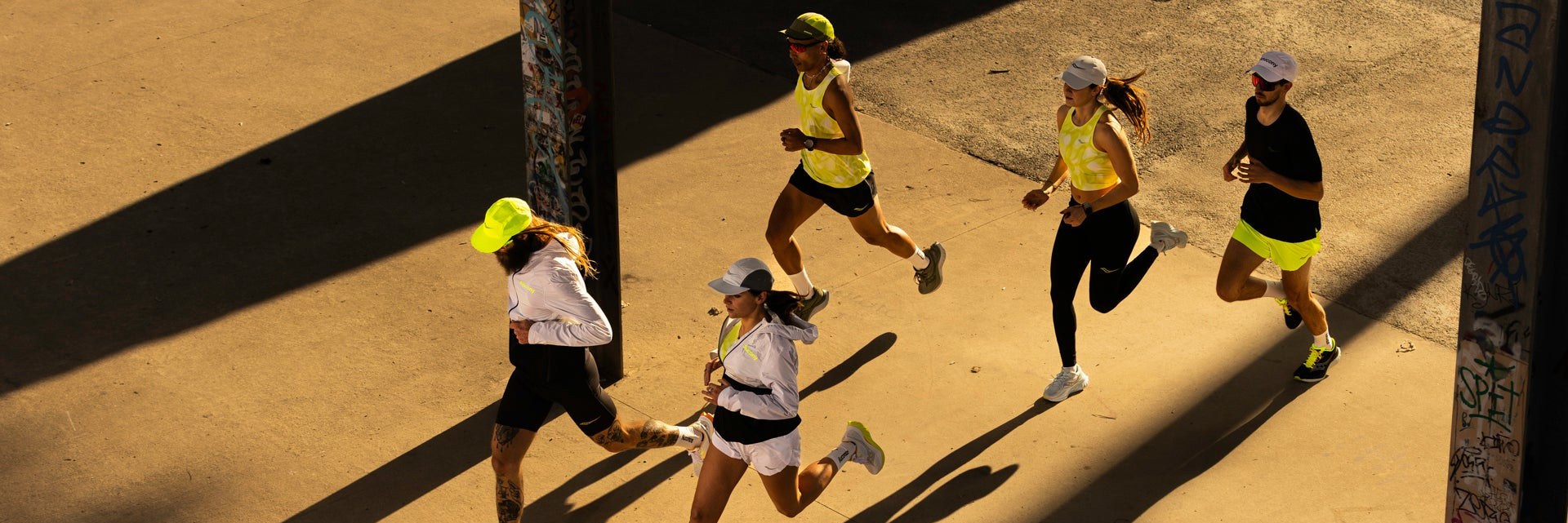 Eine Gruppe von 5 Läuferinnen und Läufern schräg von oben läuft im Sonnenlicht durch einen Säulengang